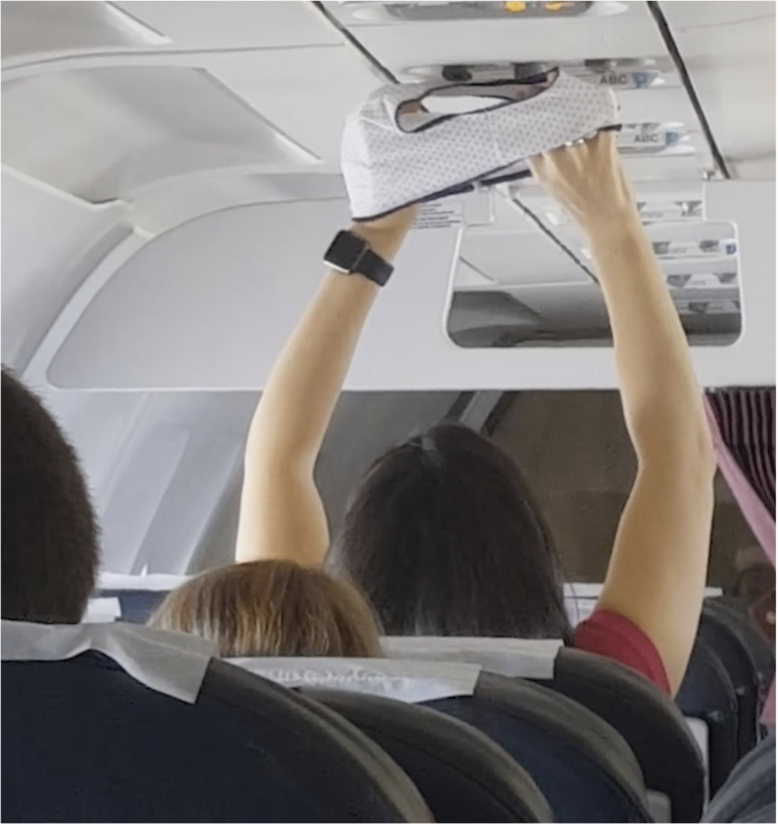 a woman on a plane holding her underwear up to the air vent