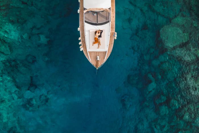 Young successful couple travel and adventure on private boat, shot from above via drone, the couple lounges on a yacht in the middle of the sea