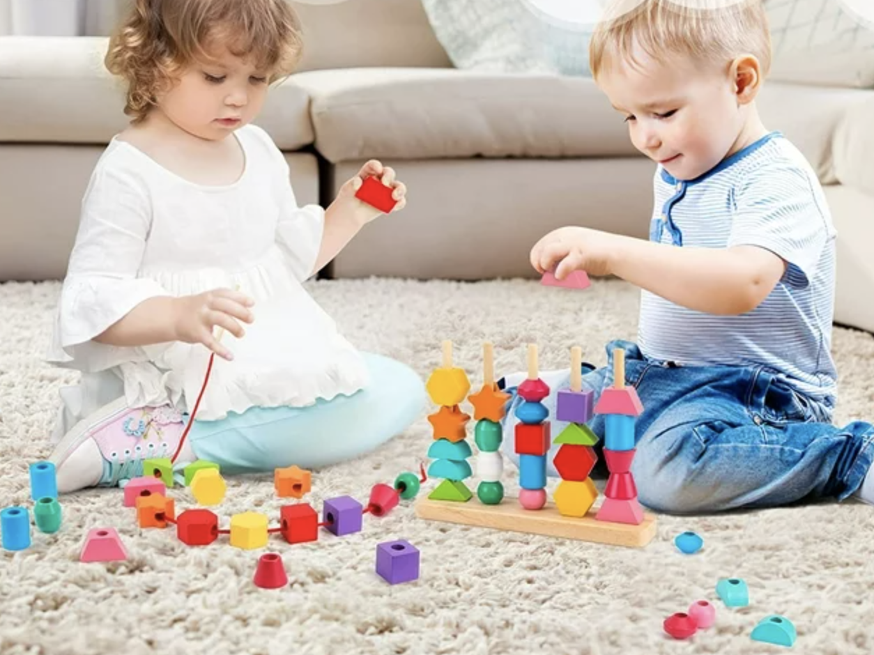 toddlers playing with colorful wooden stacking beads in different shapes