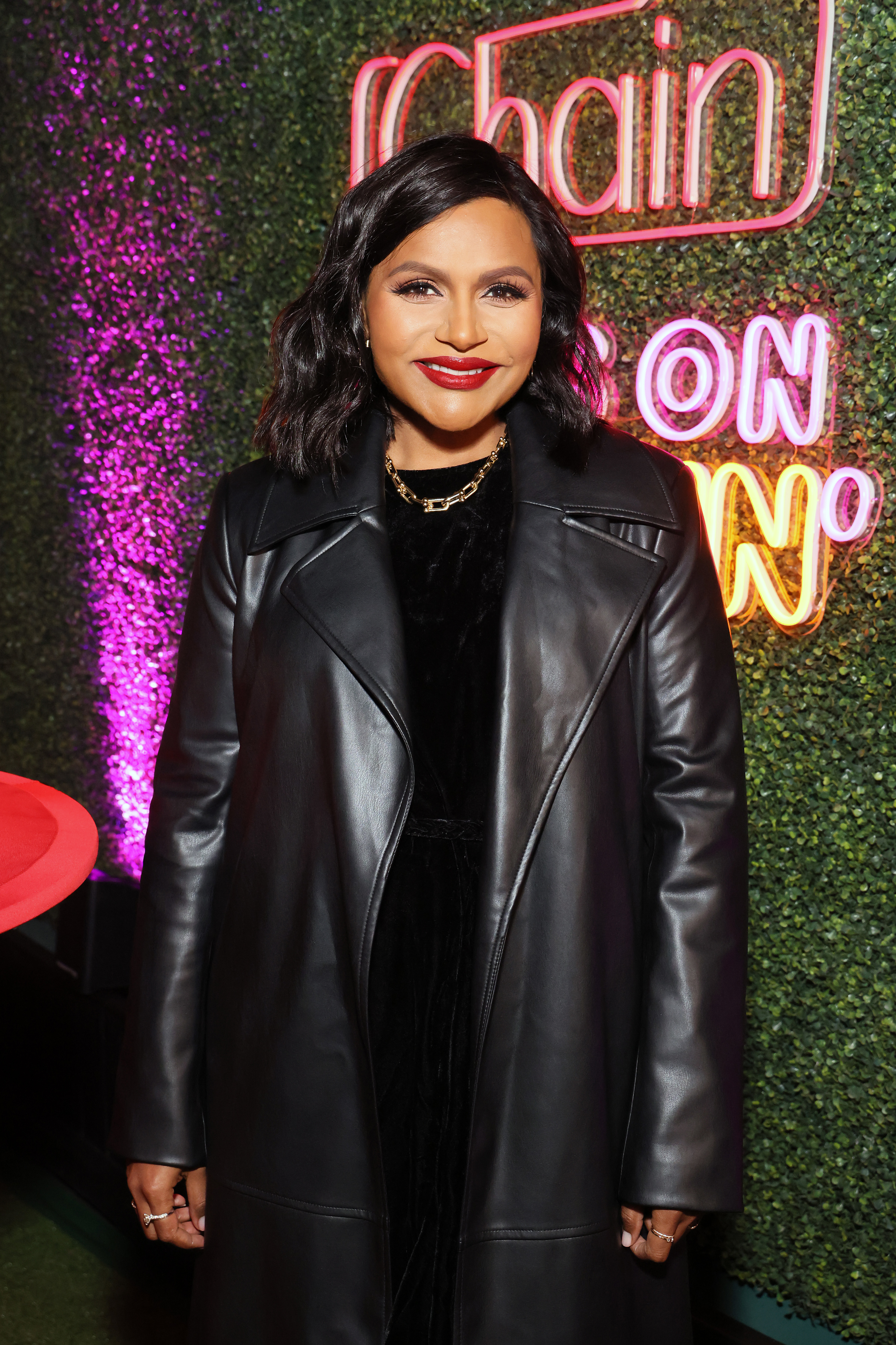 Close-up of Mindy smiling at a media event and wearing a leather coat