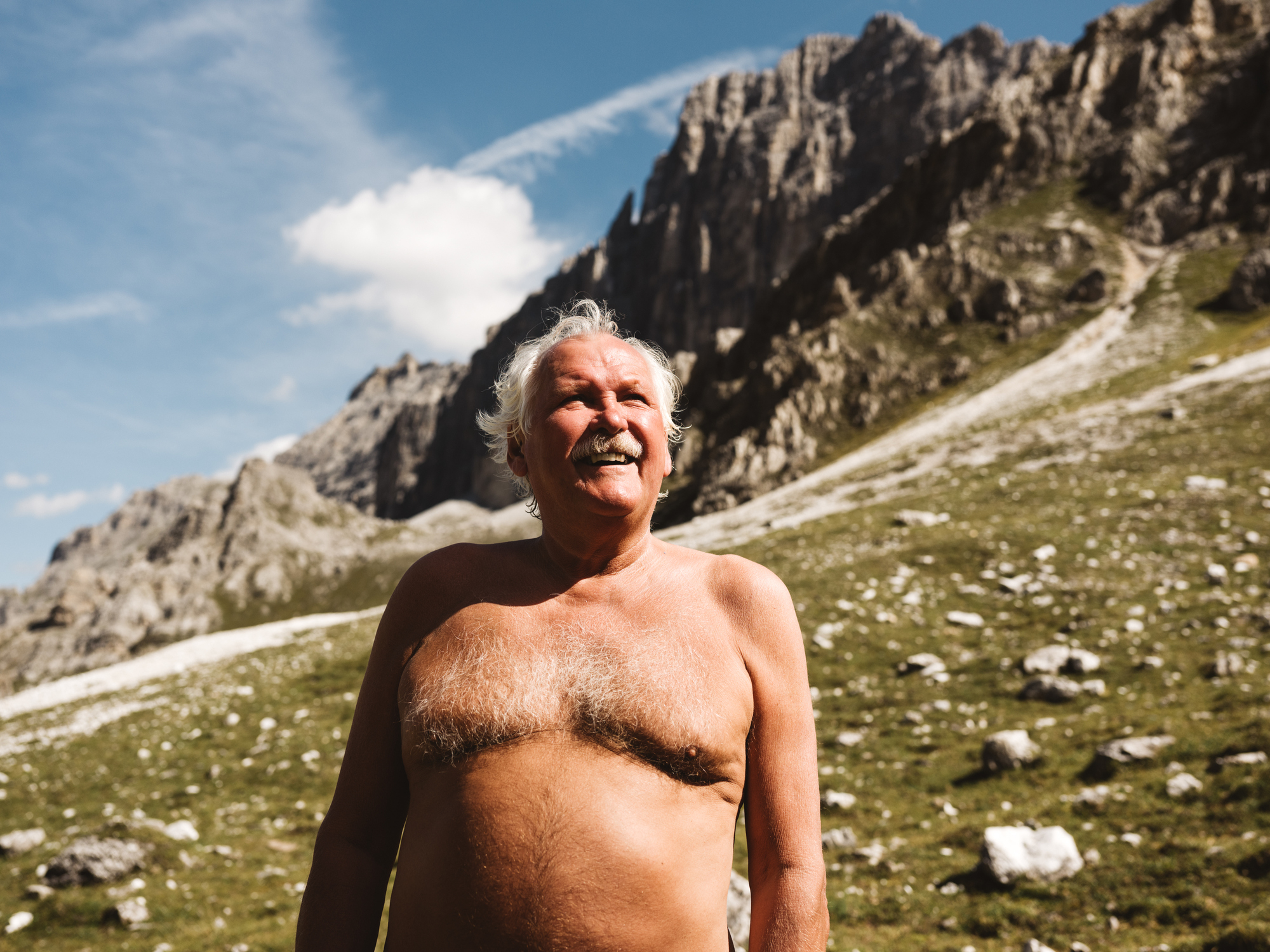 A man is standing shirtless in the mountains