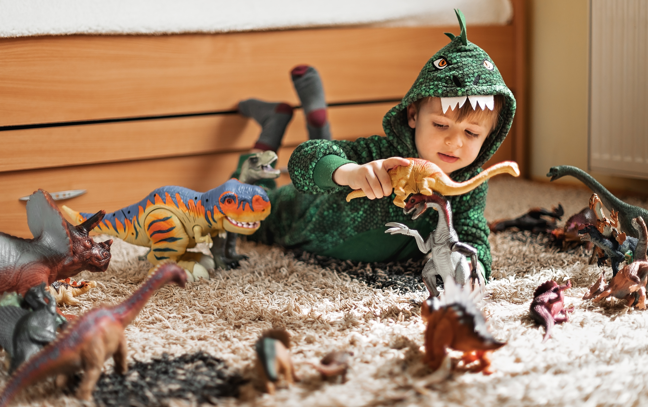 A little boy dressed as a dinosaur and playing with dinosaur toys
