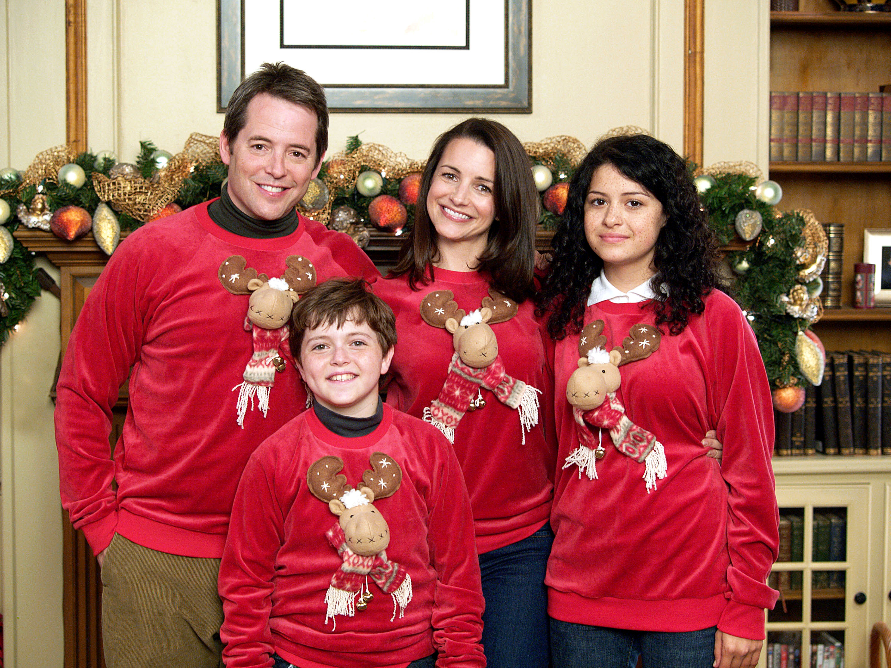 a family wearing matching red velvet christmas sweaters with a reindeer on the front of them