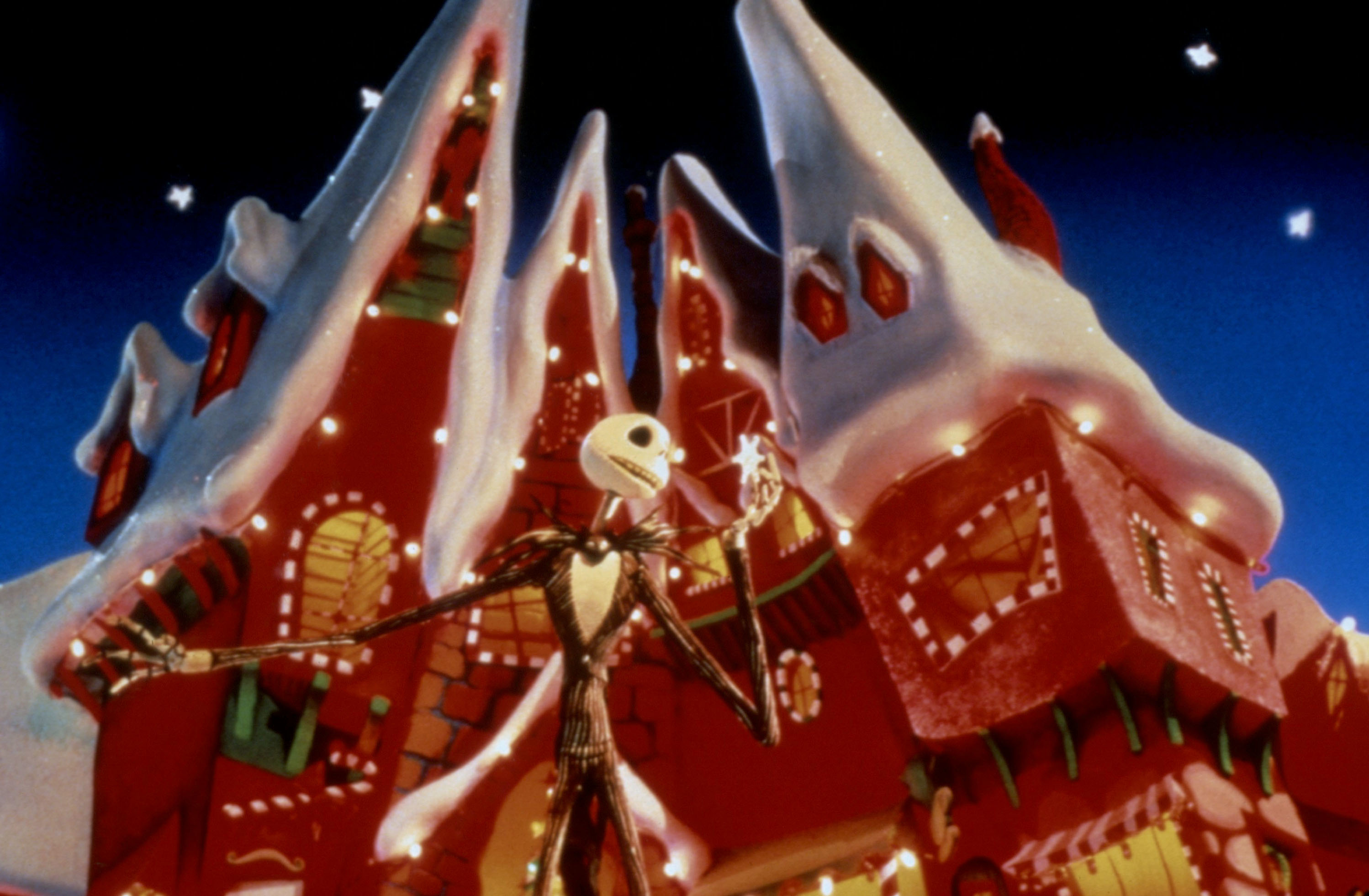 Jack Skellington standing in front of a snow covered christmas house with lights and candy cane window trimmings