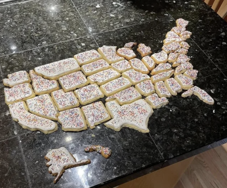 Frosted sugar cookies with sprinkles that are all in different shapes and form the map of the United States when put together