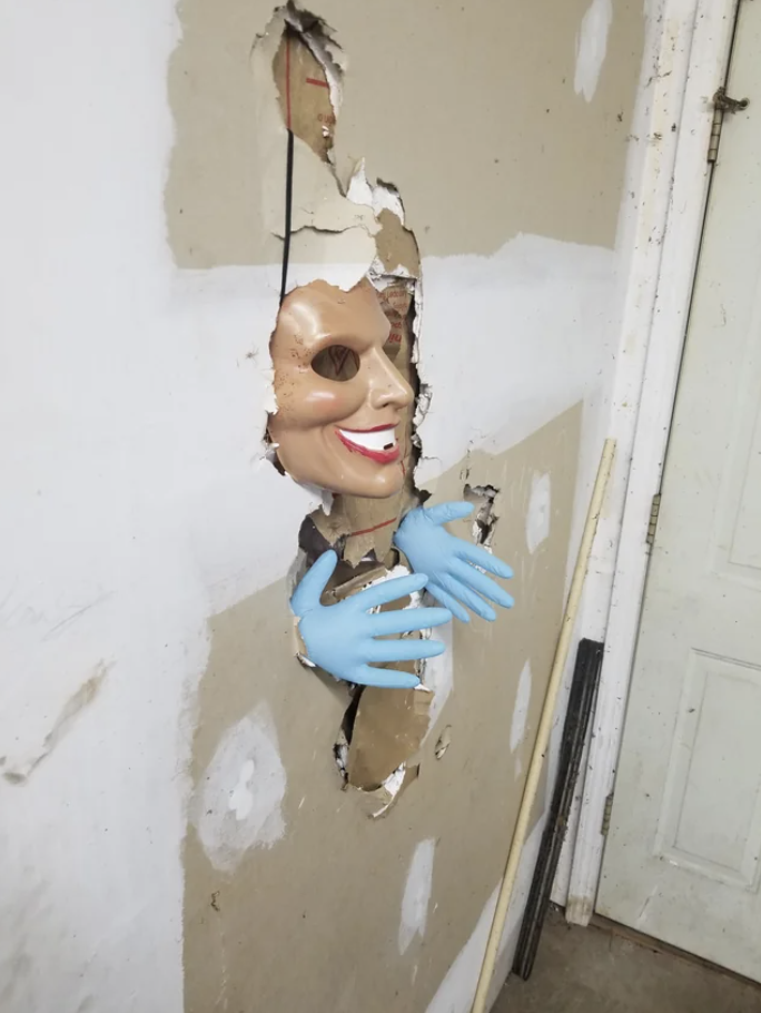 a scary mask and hands coming out of a hole in the wall