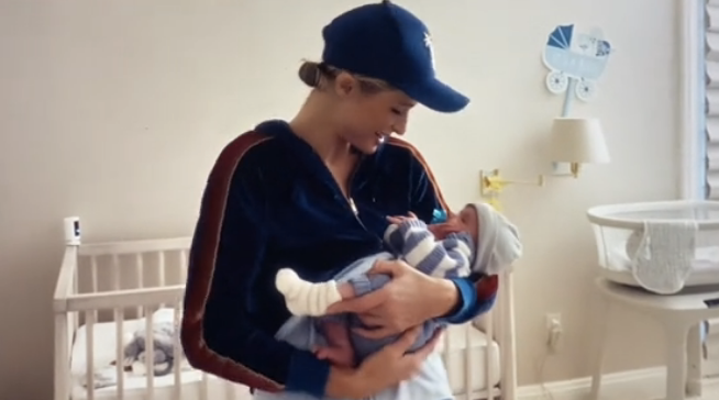 Paris wearing a cap and holding her baby in front of a crib