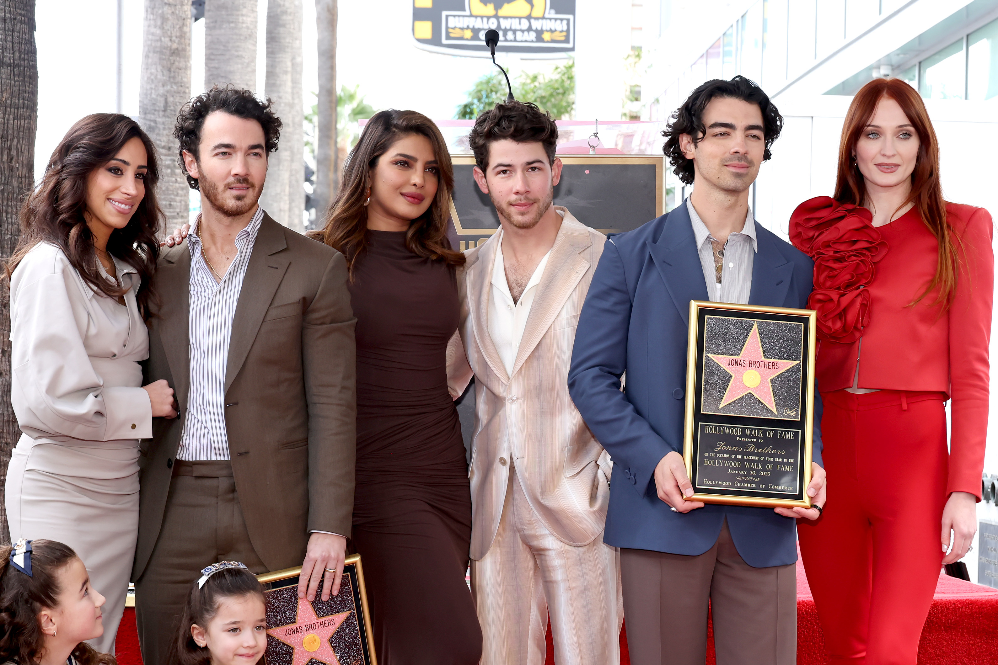 The Jonas Brothers standing with their partners at a media event