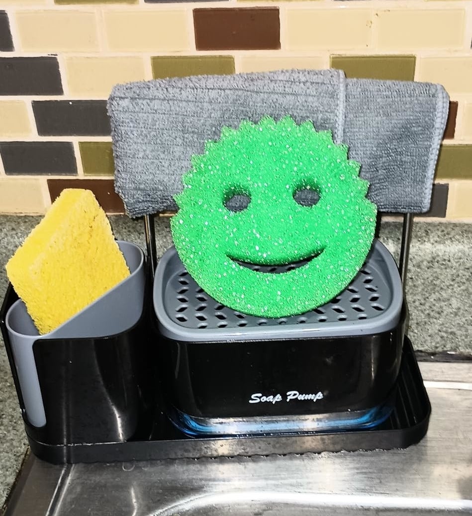 a green Scrub Daddy on a sponge-drying rack that&#x27;s placed on the upper corner of a stainless steel sink