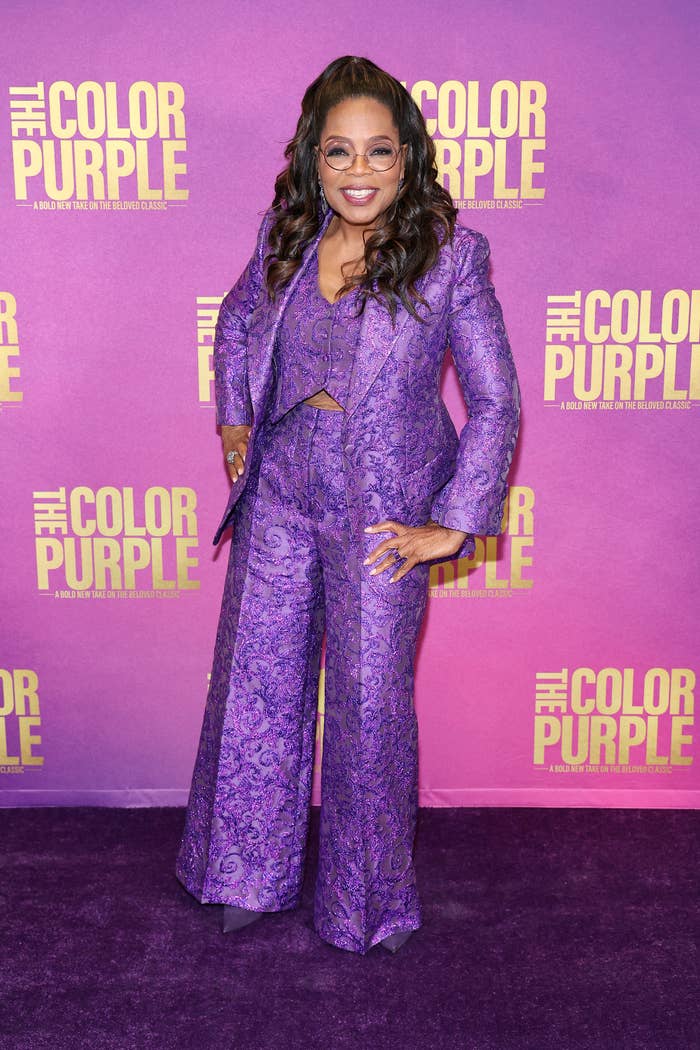 Oprah smiling and wearing a purple paisley pantsuit at an event for The Color Purple movie