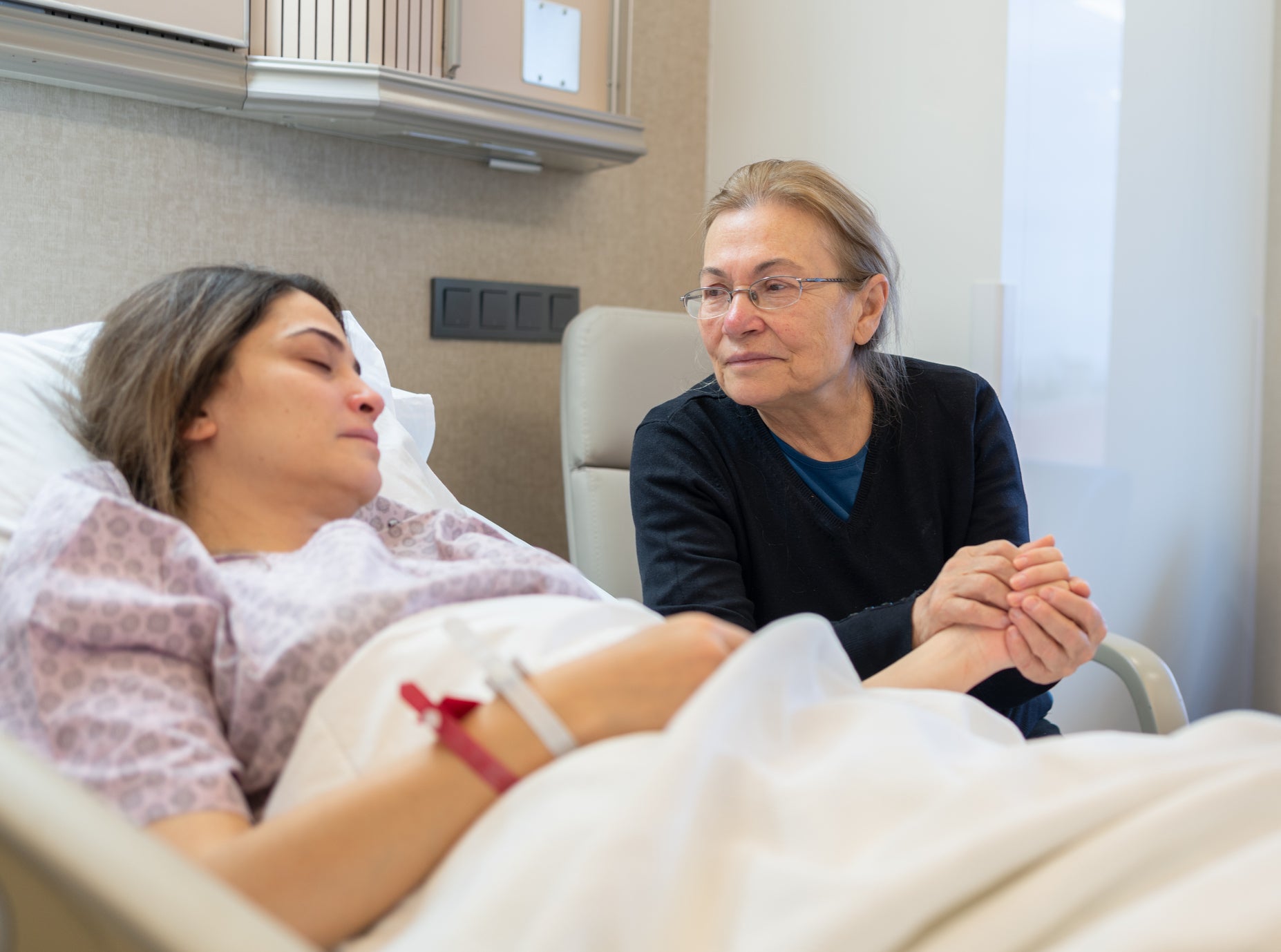 woman by the hospital bedside of her daughter, holding her hand