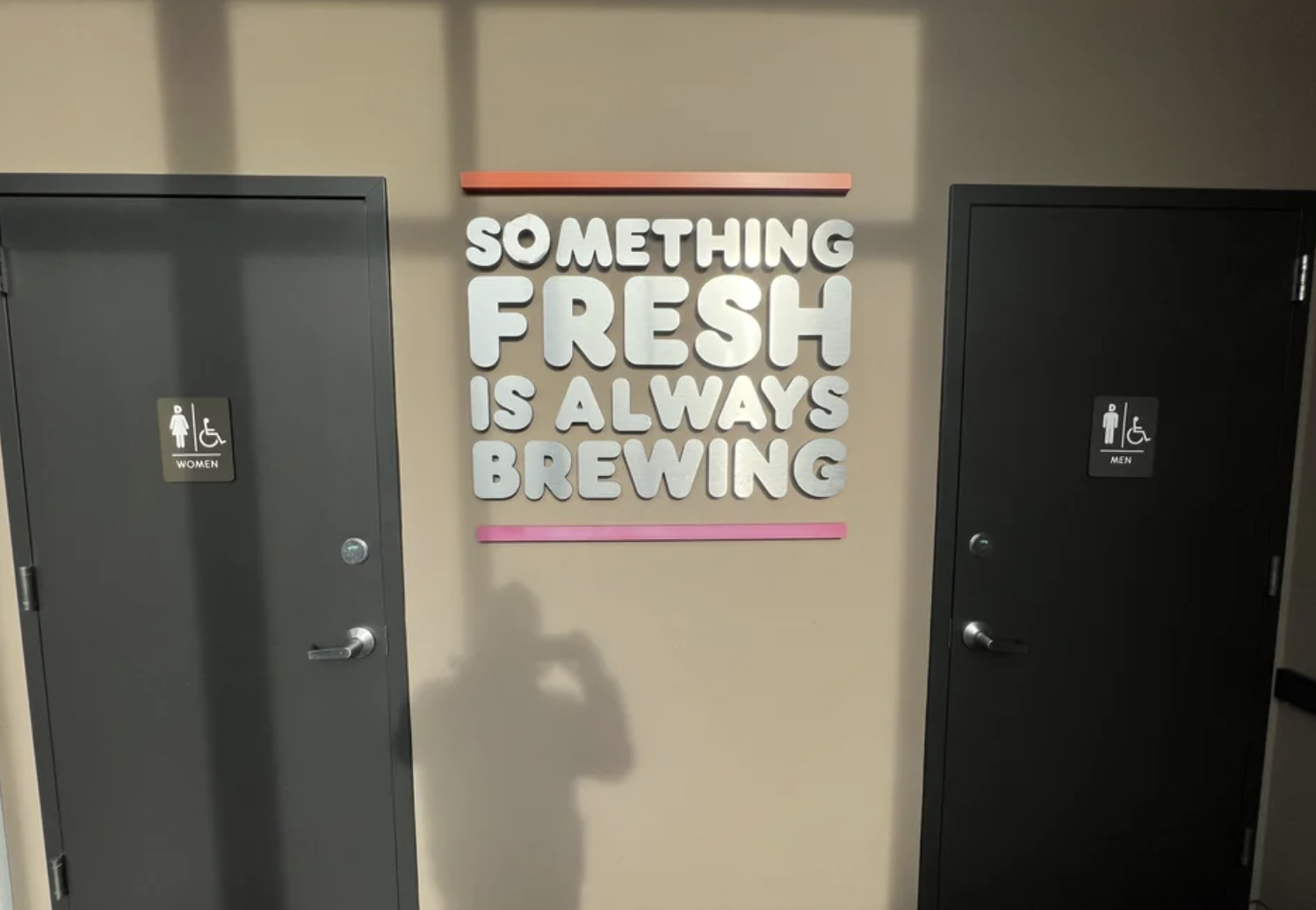 sign in the middle of two bathrooms reading, something fresh is always brewing