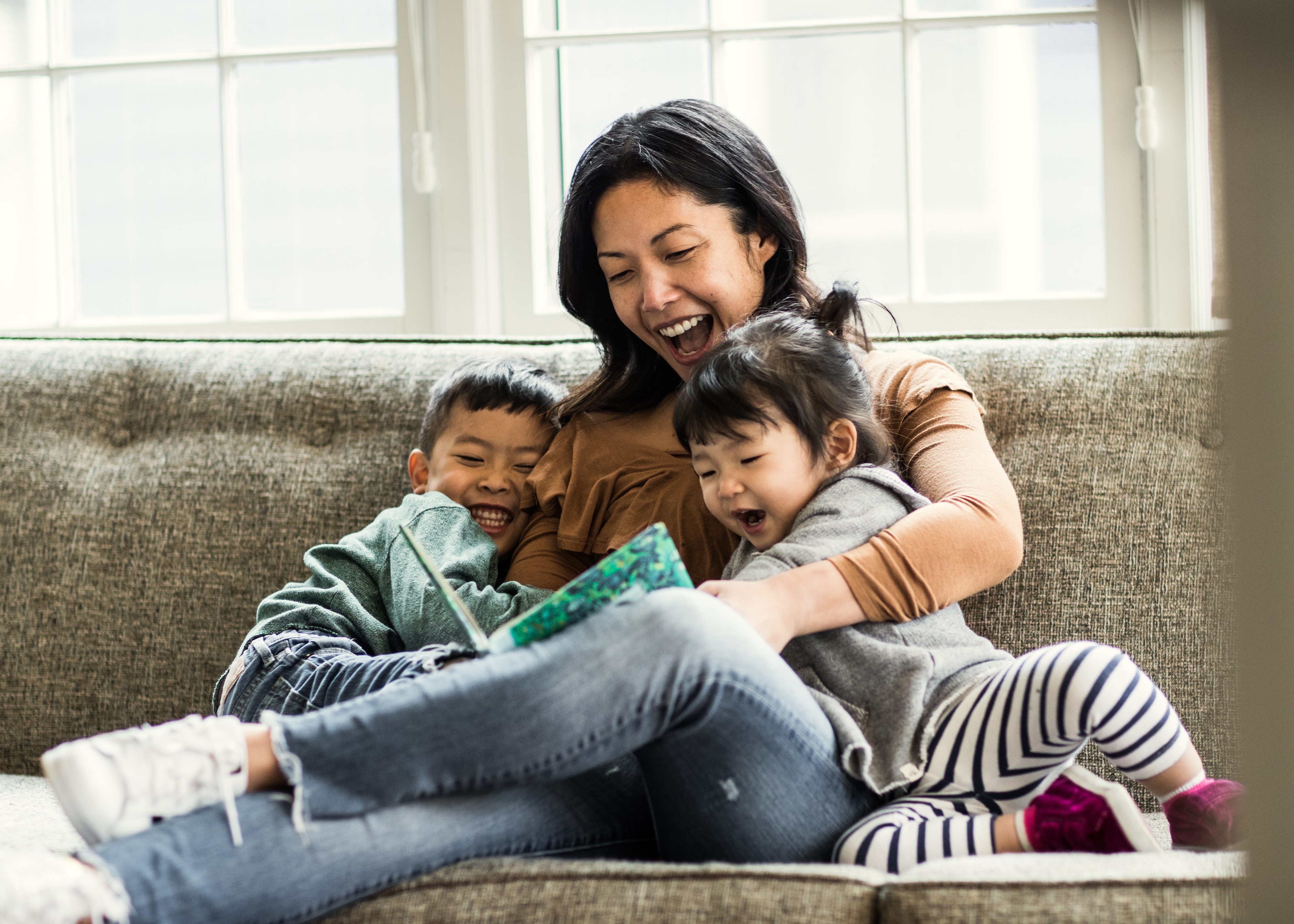 A woman sitting on the couch reading with her two little kids