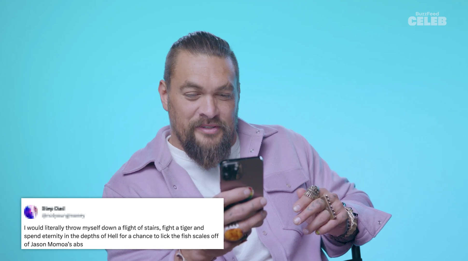 Closeup of Jason Momoa holding up a phone as he looks at the tweets
