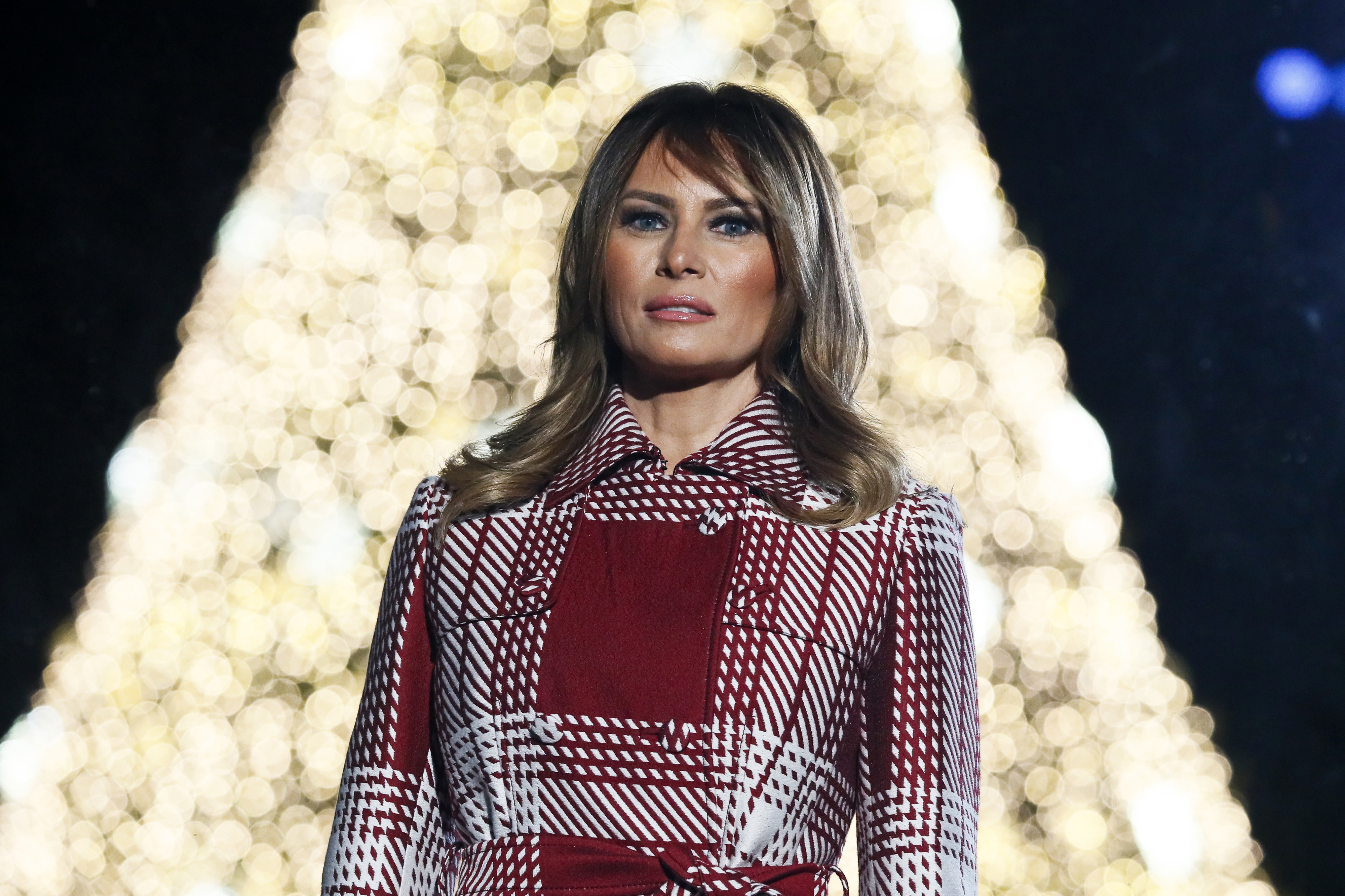 Melania in a plaid coat in front of a lit Christmas tree