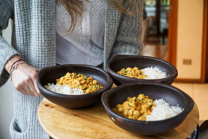 A woman serving bowls of chickpea curry over rice