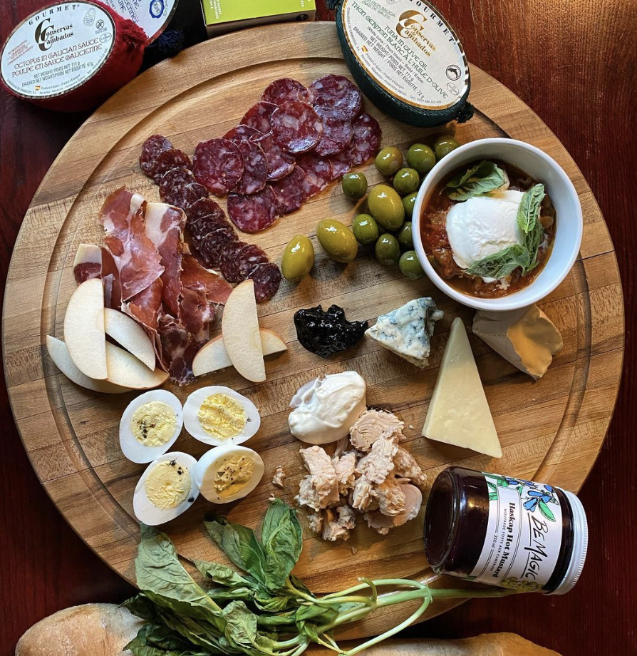 A circular charcuterie board features different meats, cheeses, eggs, olives, and sauces.