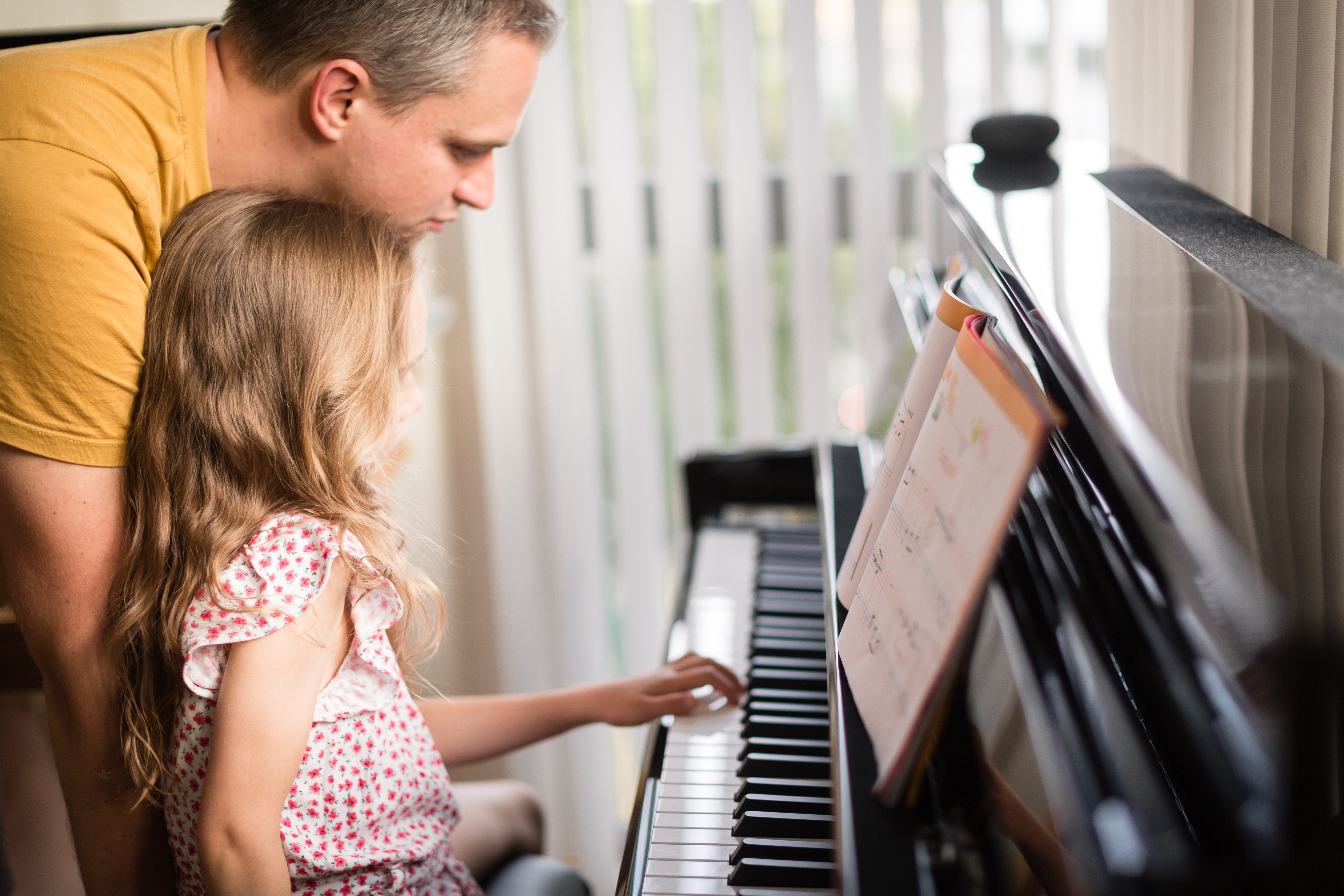 little girl playing a piano with her instructor or parent behind her