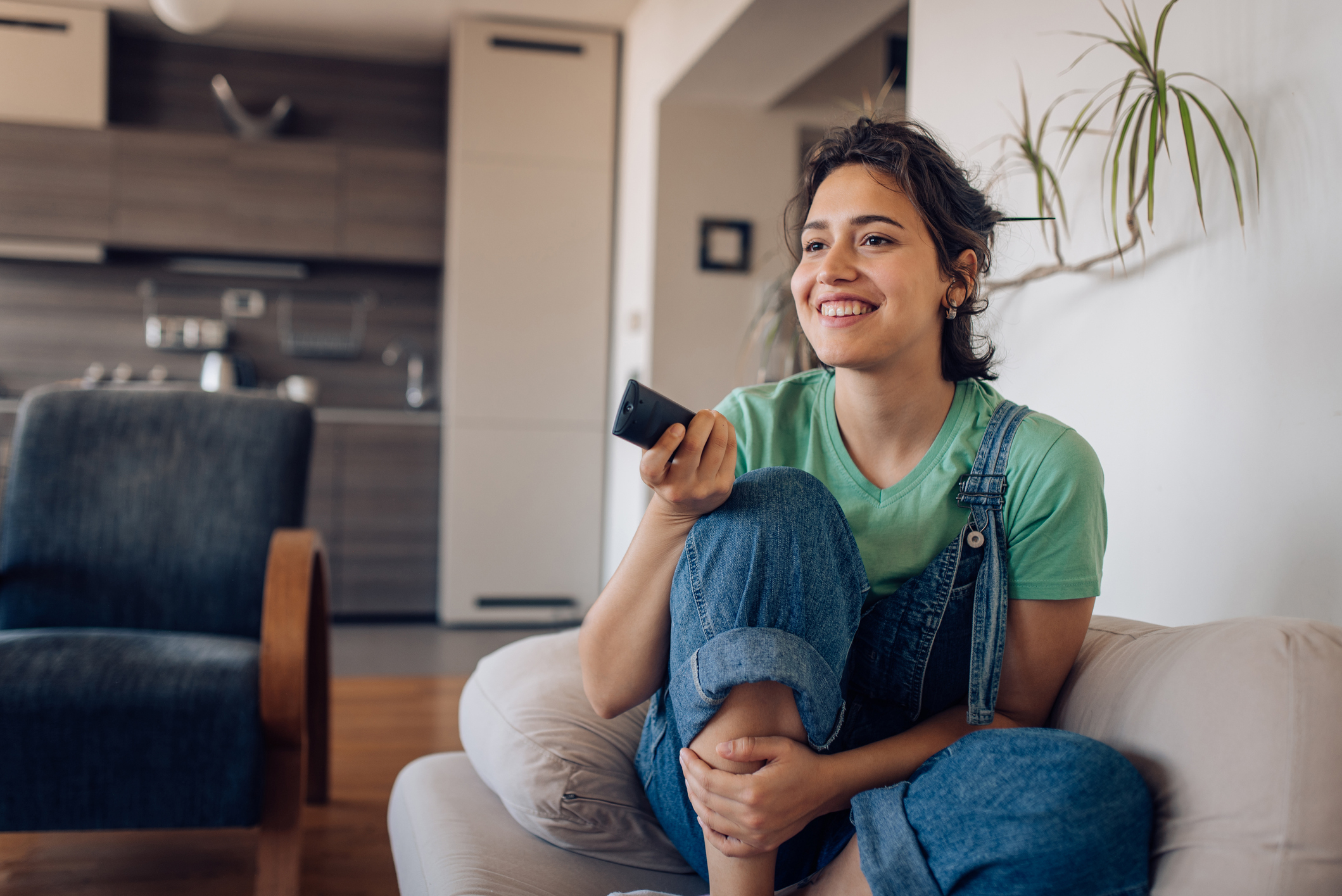 teen girl in overalls sitting on the couch with a tv remote
