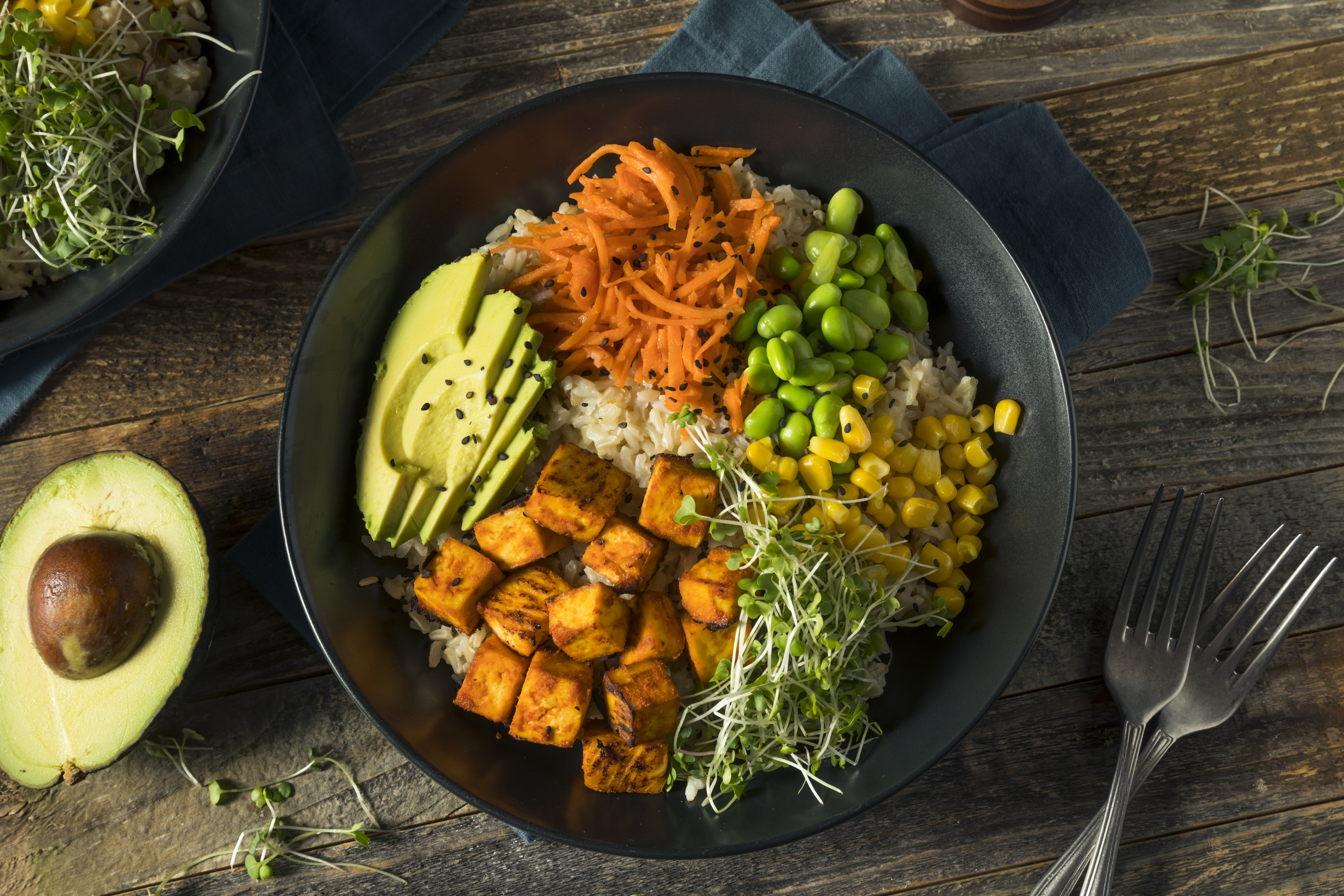 A rice bowl with tofu, avocado, corn, carrots, and edamame
