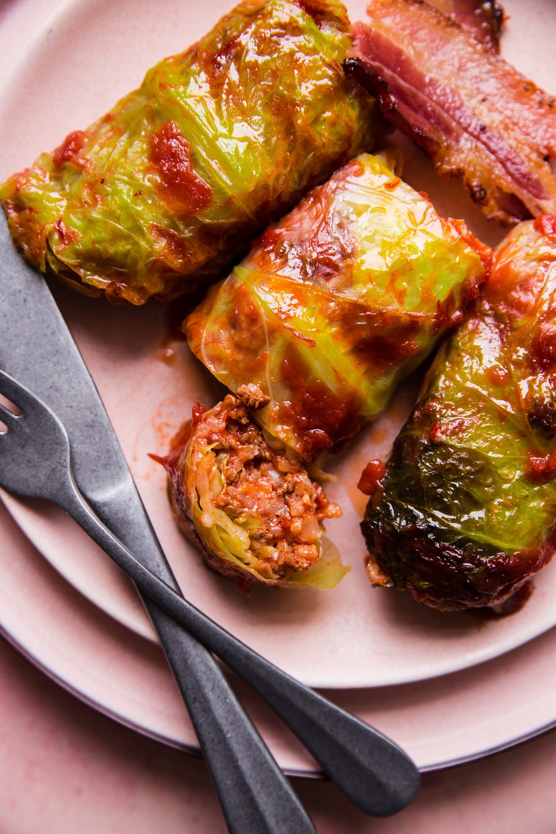 three cabbage rolls on a plate with a strip of bacon