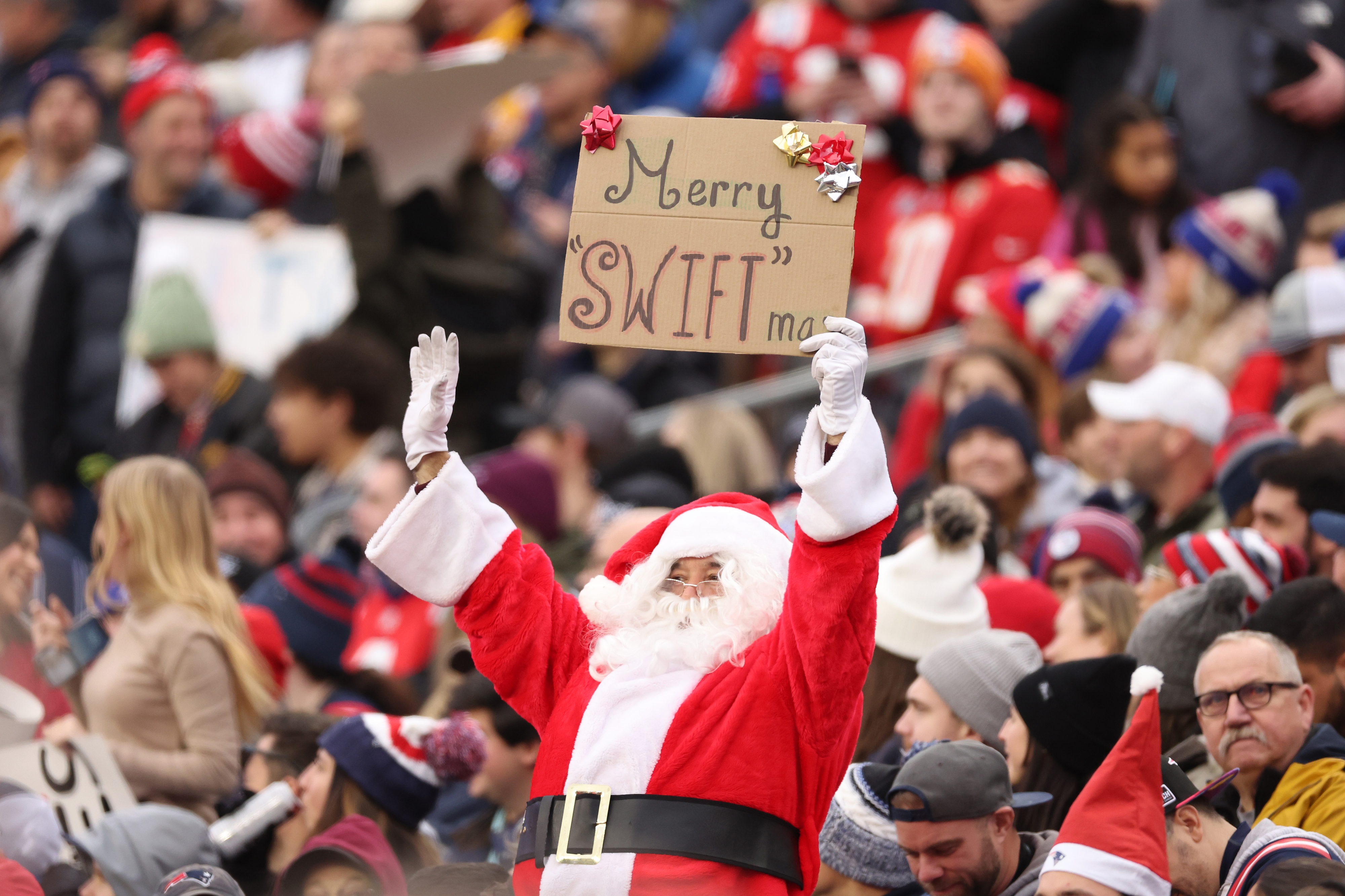 Someone in a Santa outfit holding up a &quot;Merry &#x27;Swift&#x27;mas&quot; sign in the crowd