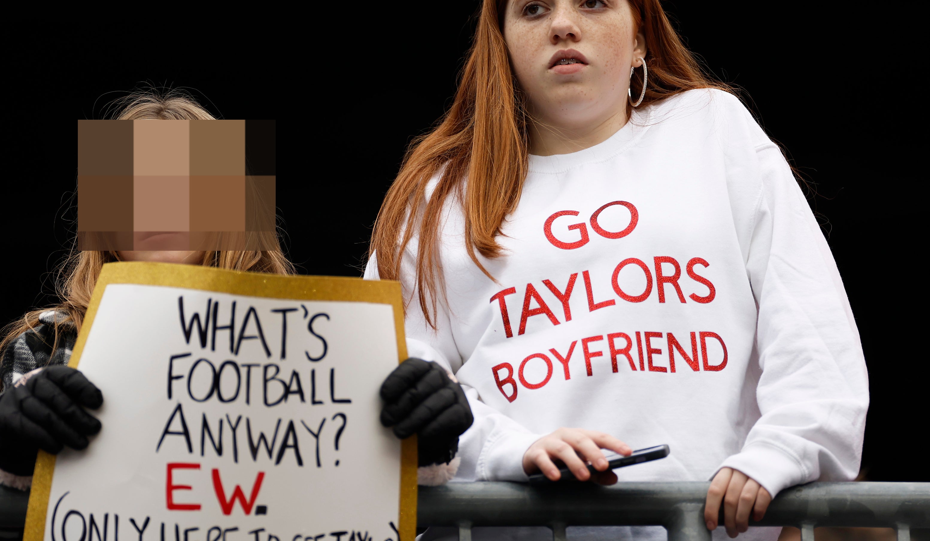 Close-up of someone holding the sign &quot;What&#x27;s football anyway? EW (only here to see Taylor)&quot; and someone wearing a &quot;Go Taylors boyfriend&quot; sweatshirt