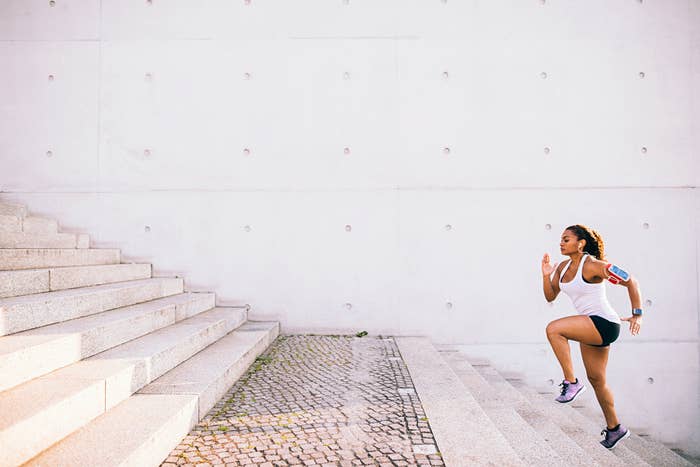 A woman working out on stairs in a city setting, with headphones in and her phone strapped to her arm in an armband