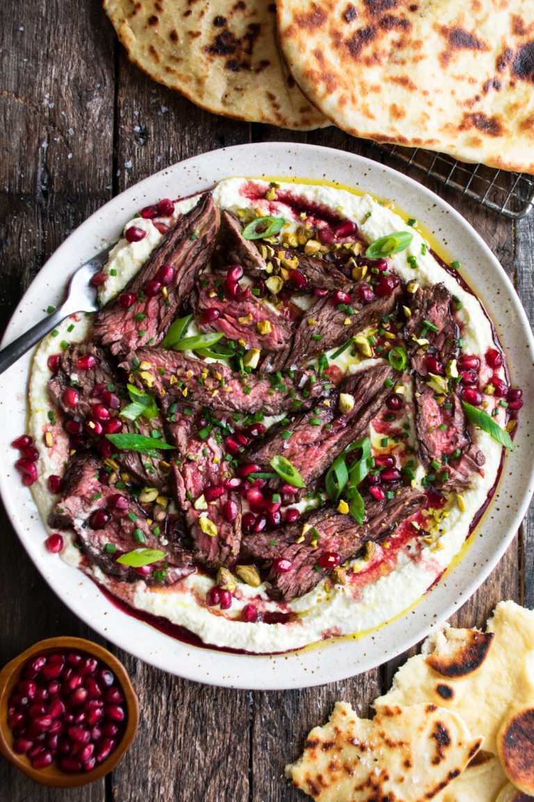 thinly sliced skirt steak on top of a bed of whipped feta and topped with pomegranate and scallions
