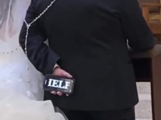 groom holding up a help message on his phone at the alter