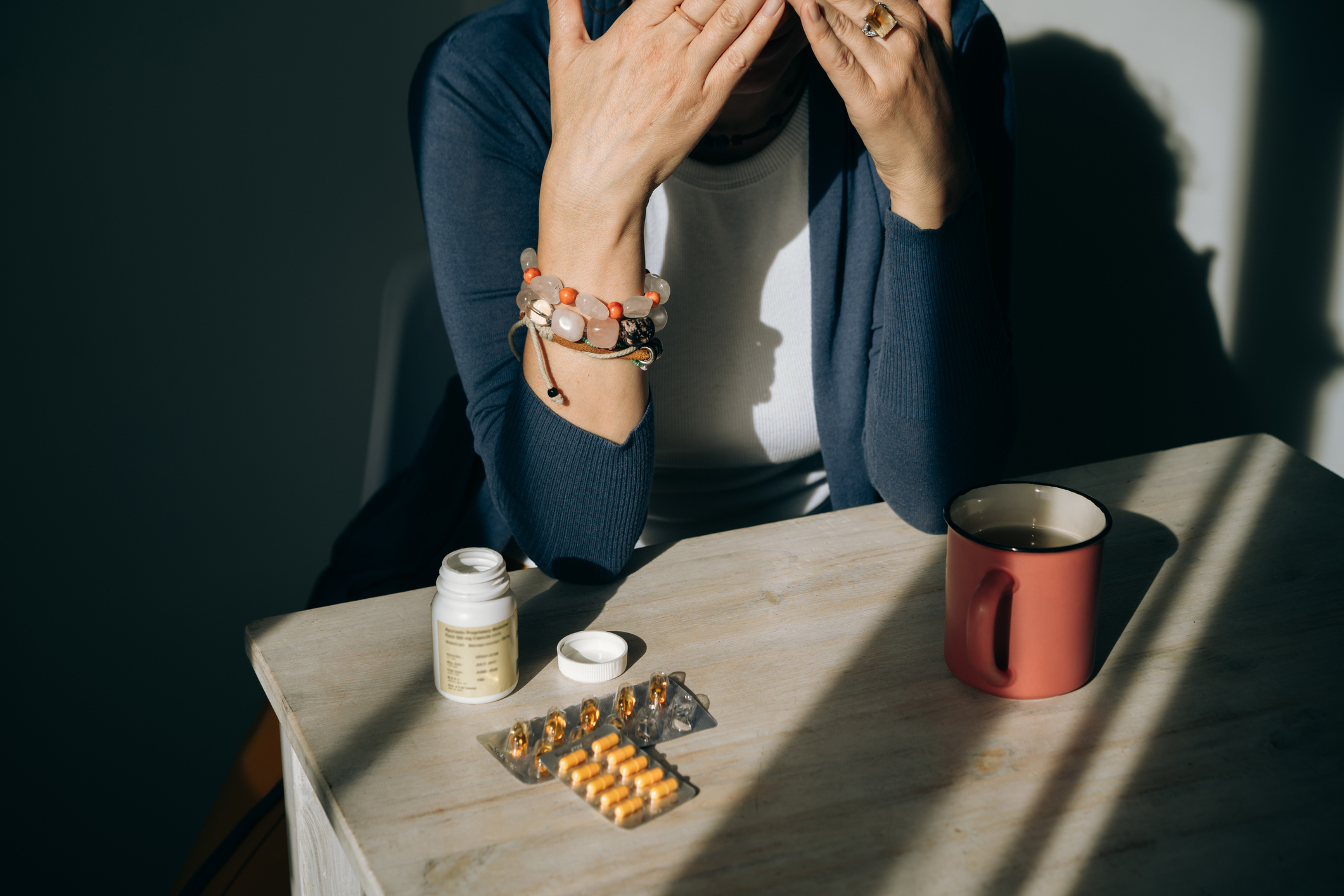 A woman standing at a table with yellow and green pills in her hand