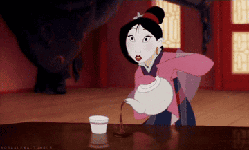 Mulan stares open mouth ahead and pours tea onto the table instead of in the mug.