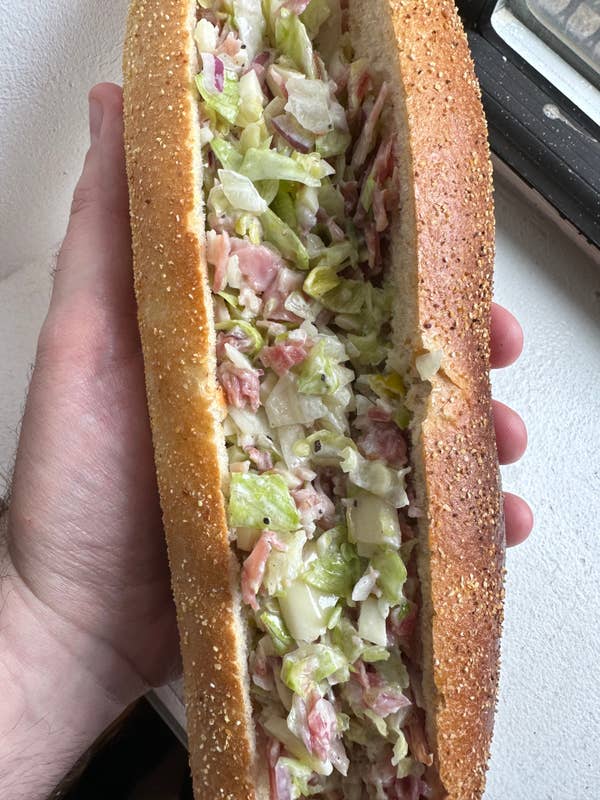 author holding a sandwich on a toasted sub roll with various chopped Italian sandwich ingredients inside