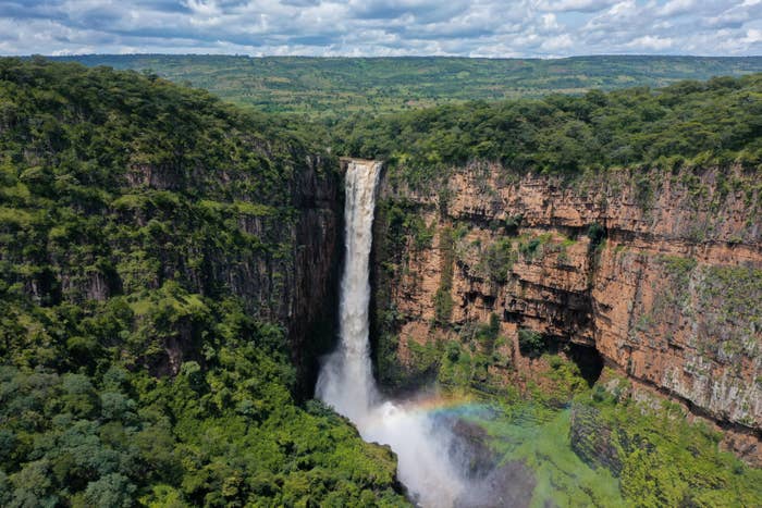aerial shot of Kalambo Falls, Zambia; a very tall, thin, powerful waterfall pours down from a high, sheer cliff face