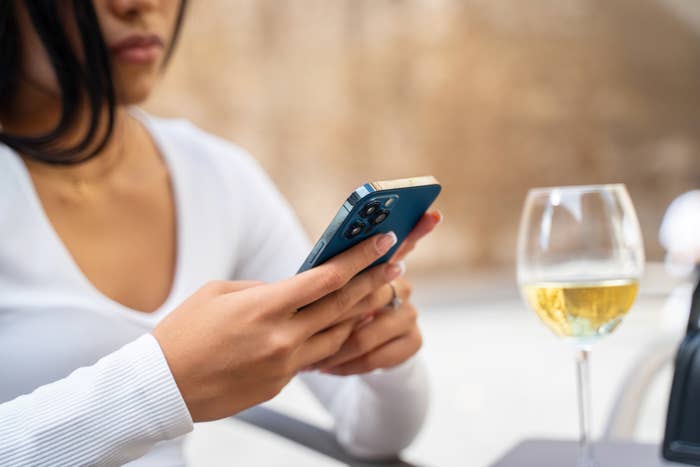 a person on her phone with a glass of wine