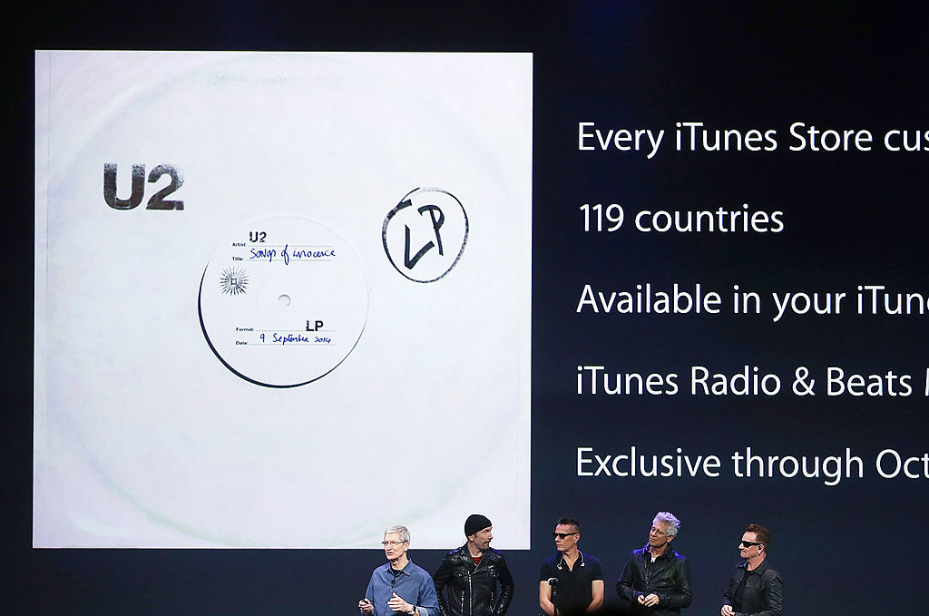 tim cook on stage with U2 with image of songs of innocence album behind them