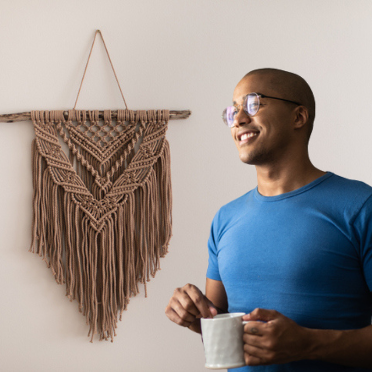 a man standing in front of macrame with coffee in his hands