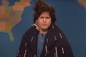 Andy Samberg squinting as though he's really tired with a comforter wrapped around him on SNL's Weekend Update