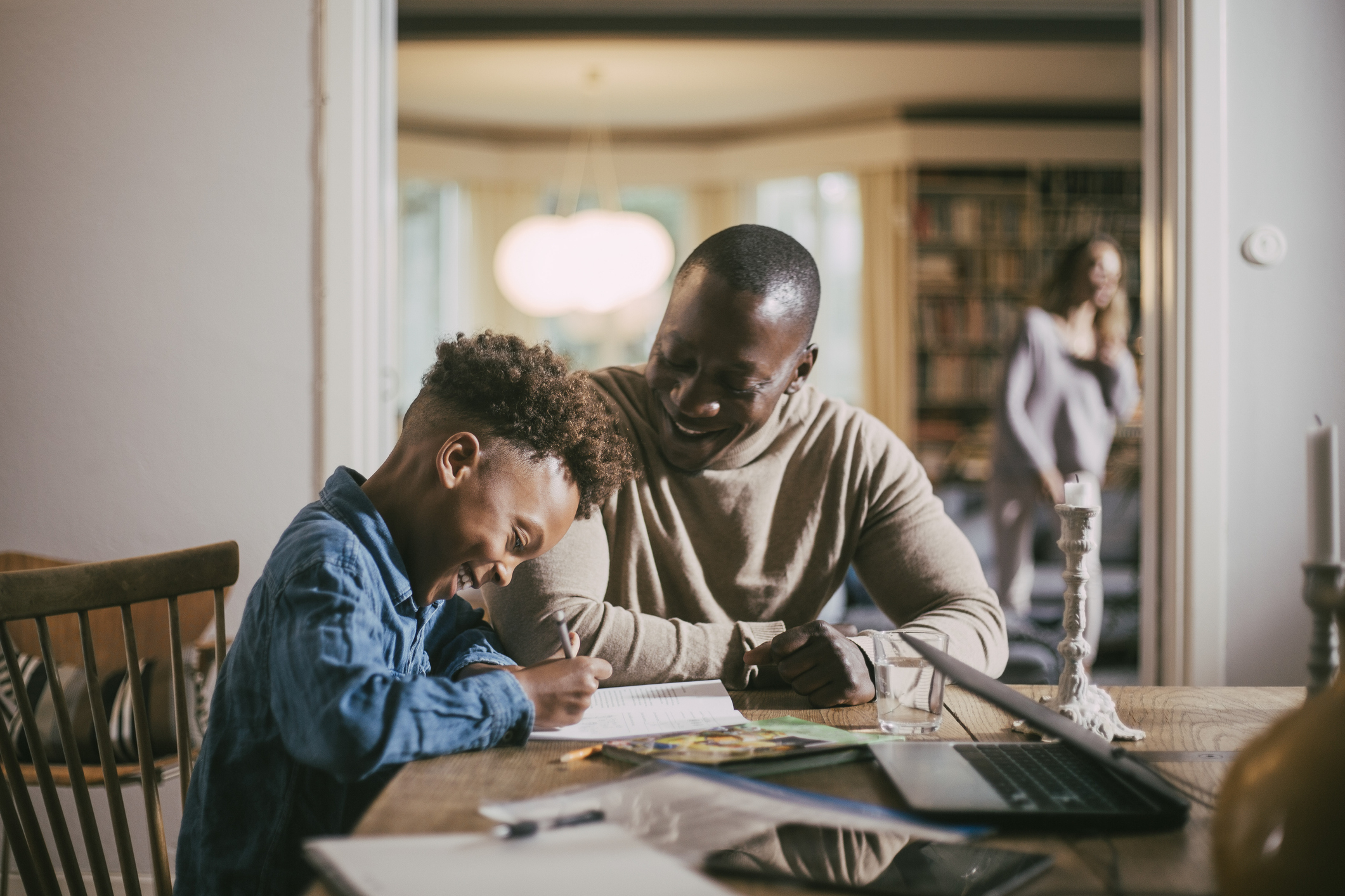 A father helps his child with homework at the dining room table