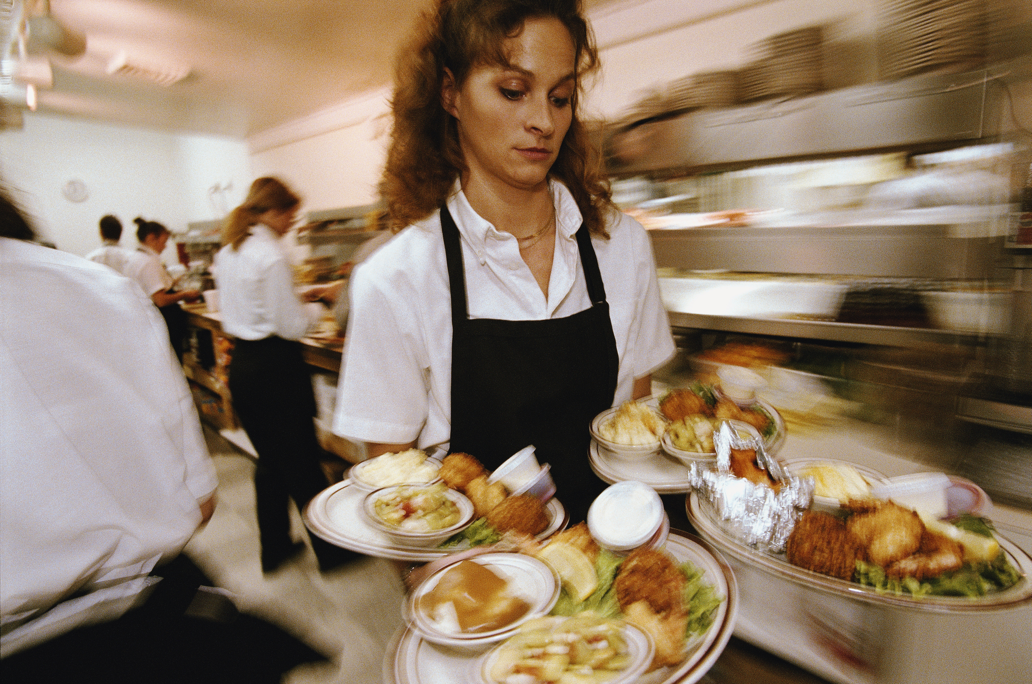 A waitress carrying multiple plates in the kitchen