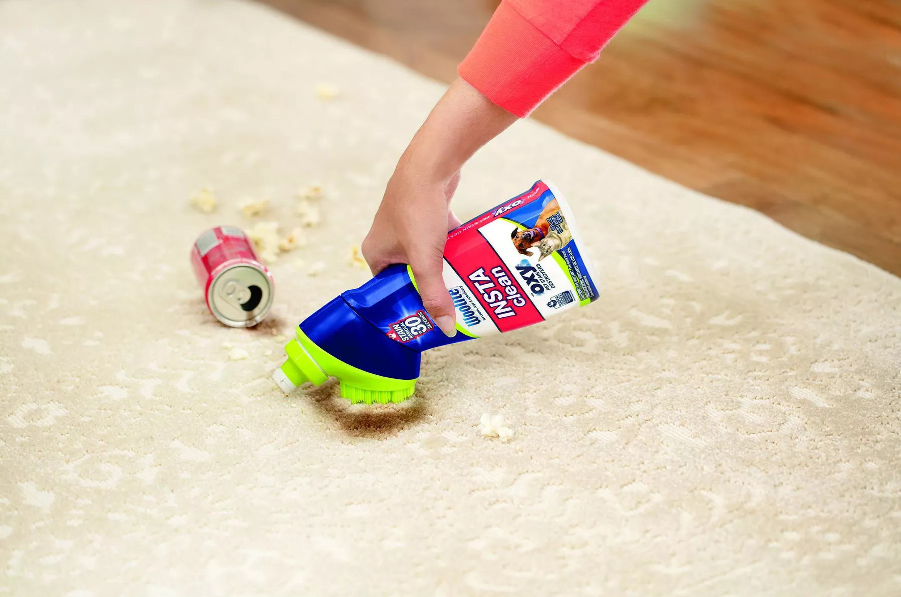 a hand applying the bottle of product, which has a built-in applicator, on a cream rug