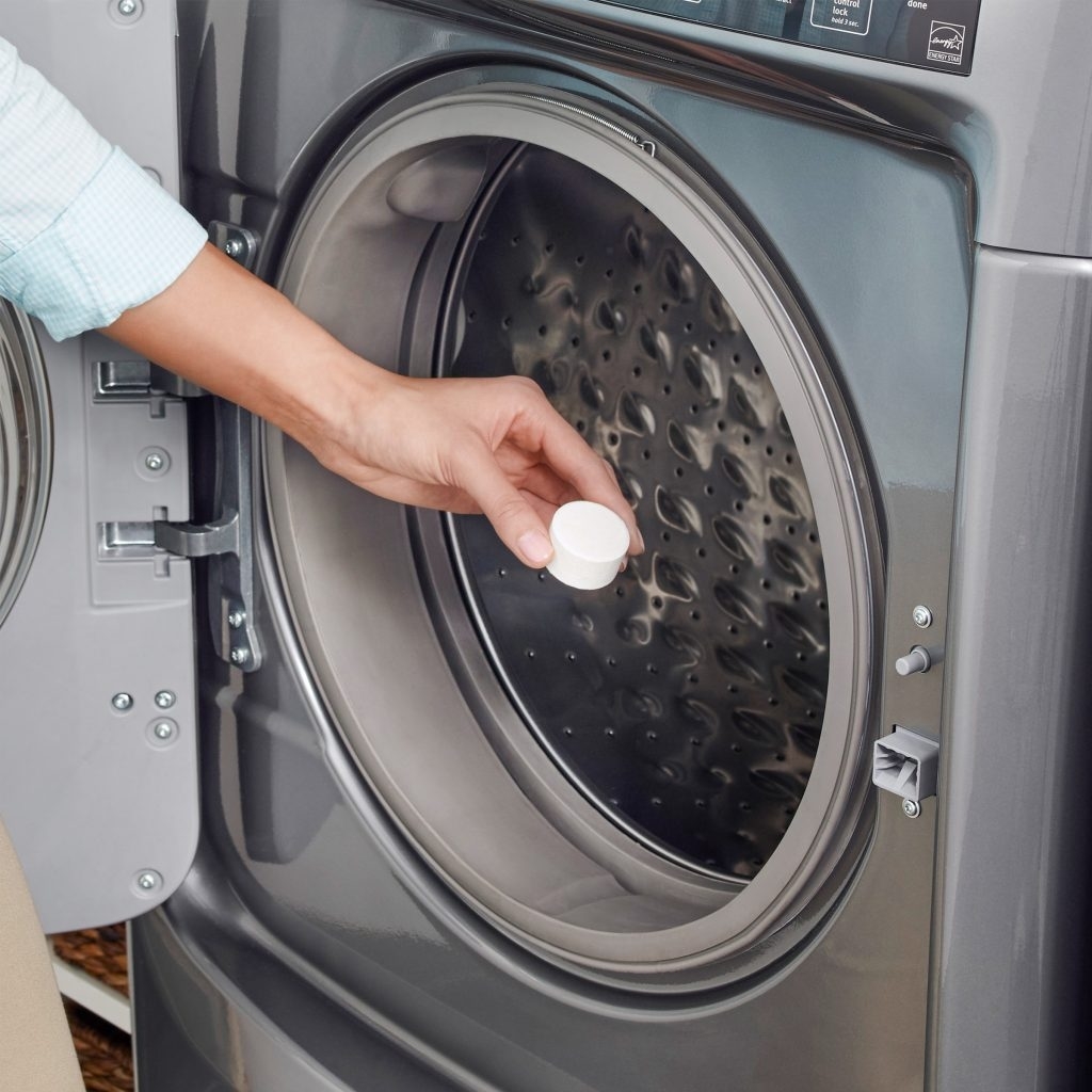 a person putting the product, a white tablet, into a front-loading washer drum