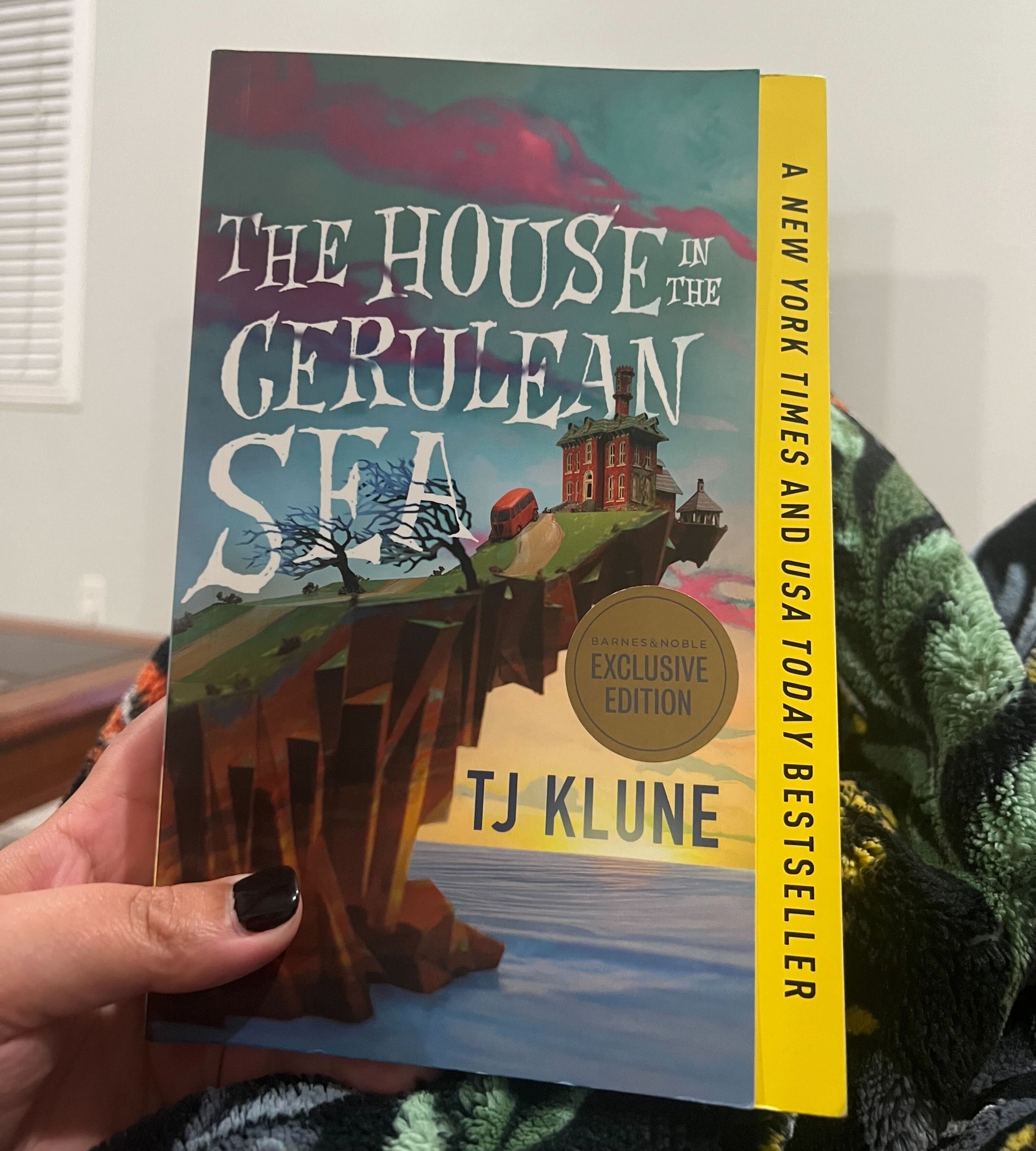 The author is holding a copy of &quot;The House in the Cerulean Sea&quot; by TJ Klune