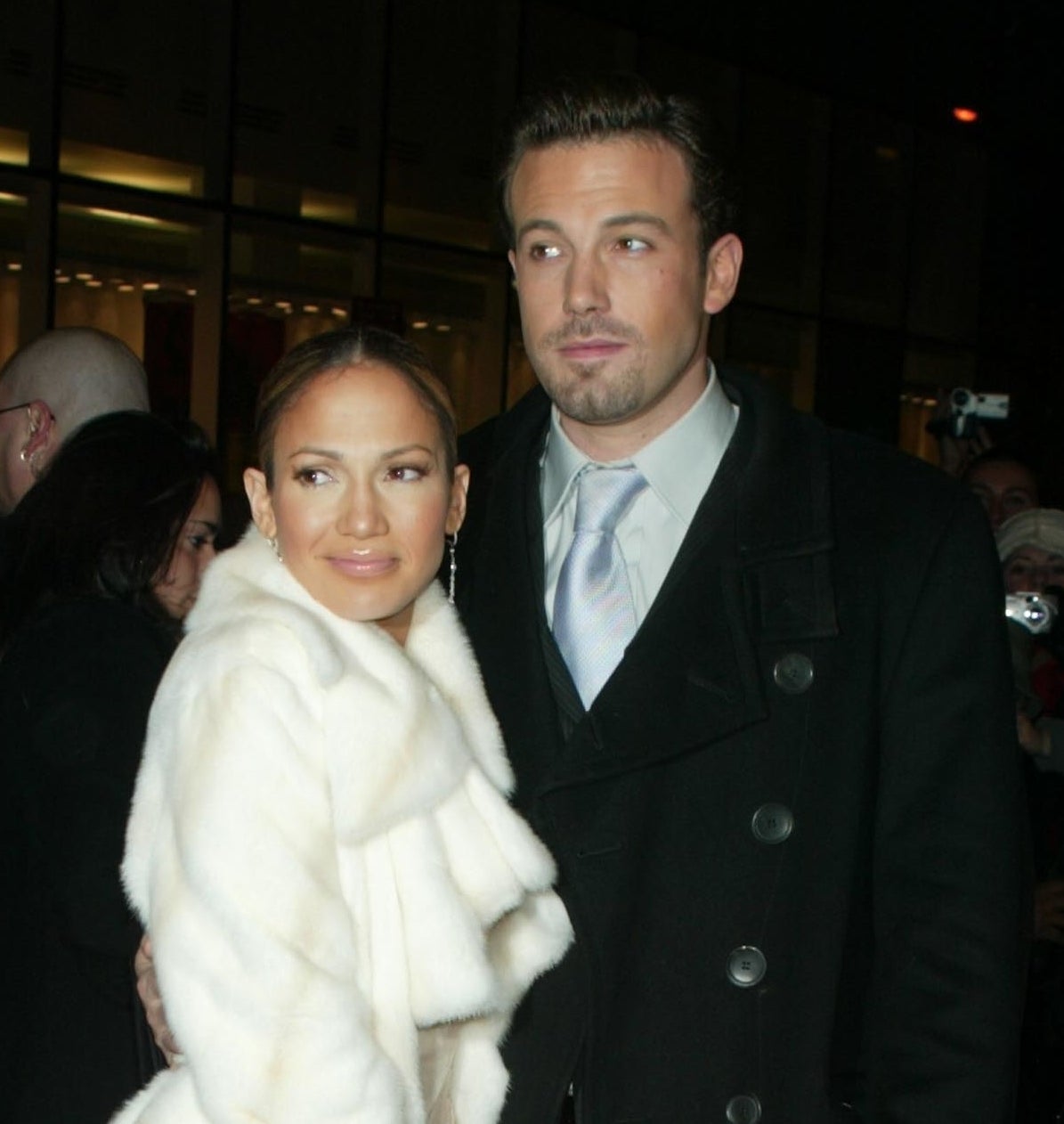 Close-up of JLo in a furry jacket and Ben in a suit and tie and his arm around her
