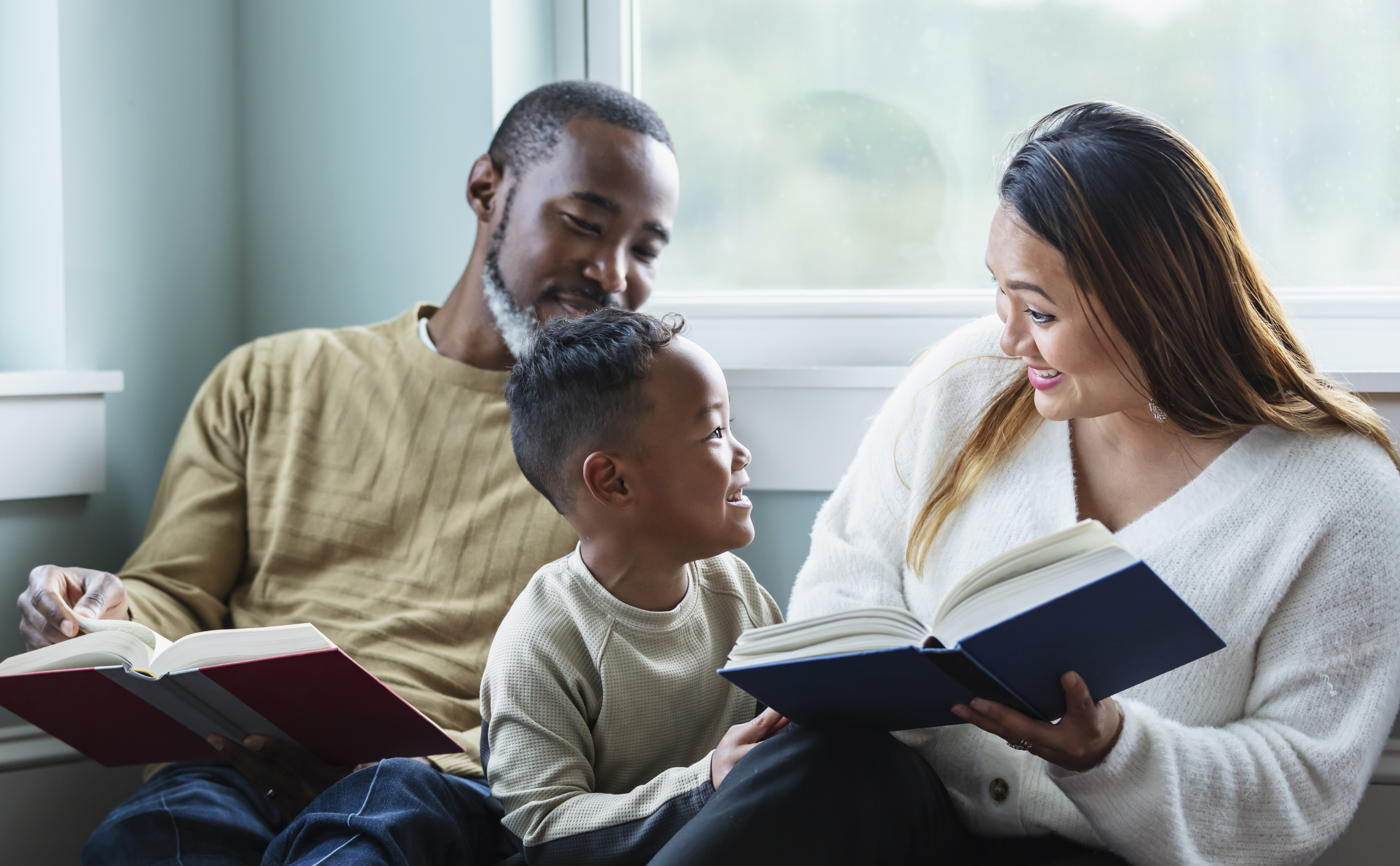 two parents reading a book while happily looking at their child