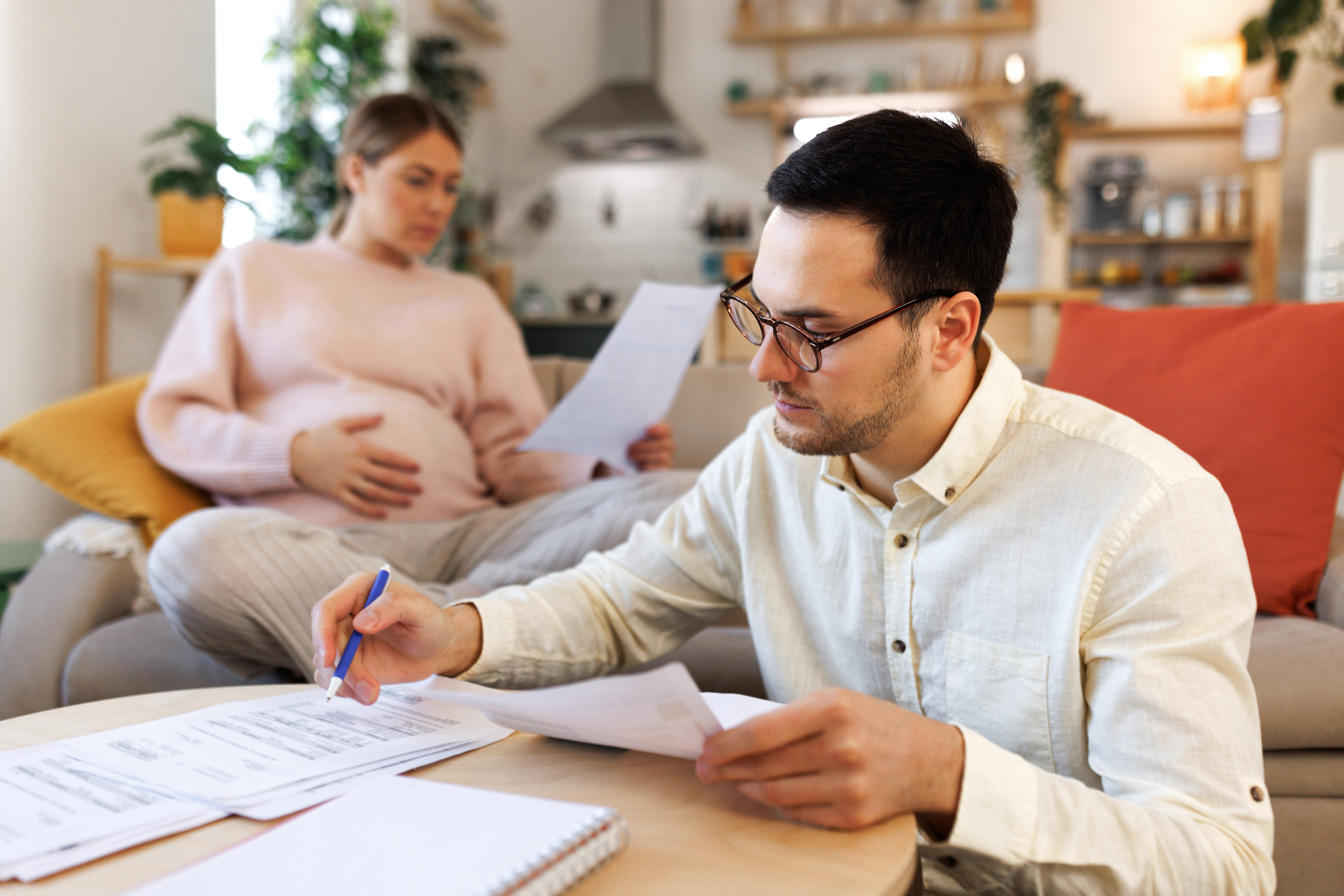 a pregnant woman in the background as her husband fills out paperwork