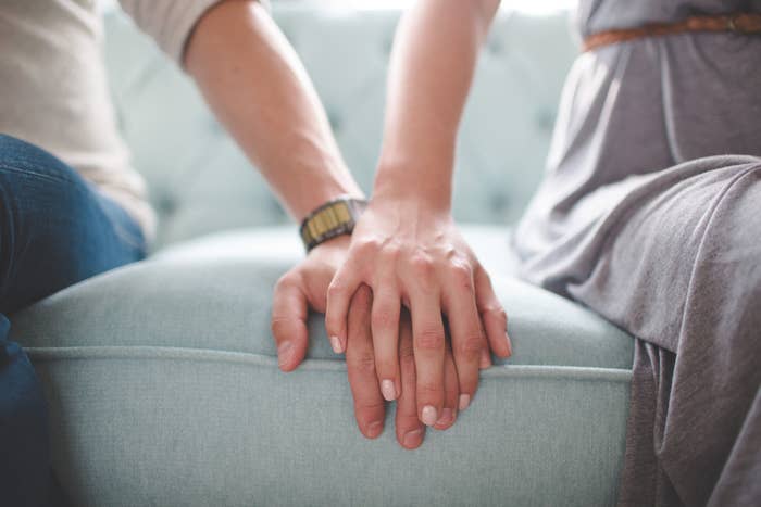A couple with their hands together on the couch