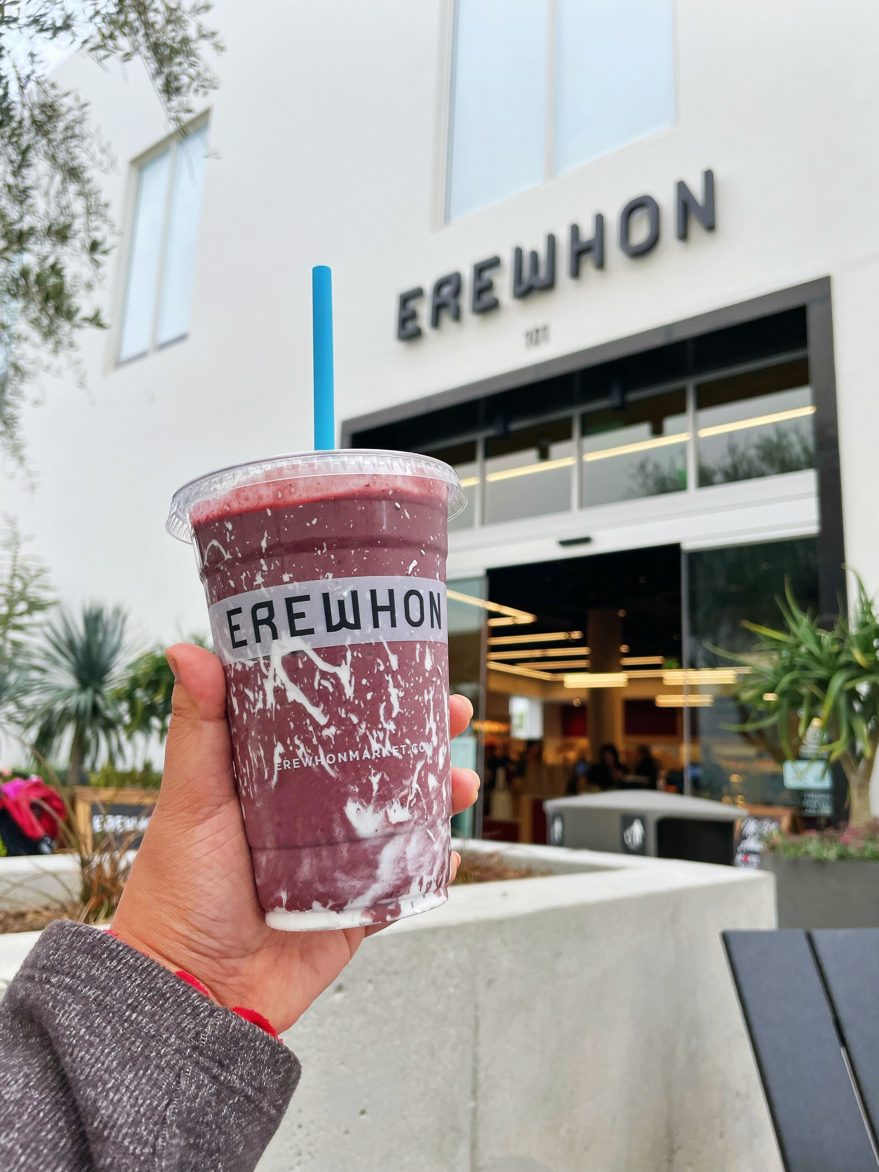 The author is holding up an Erewhon smoothie in front of the Erewhon store