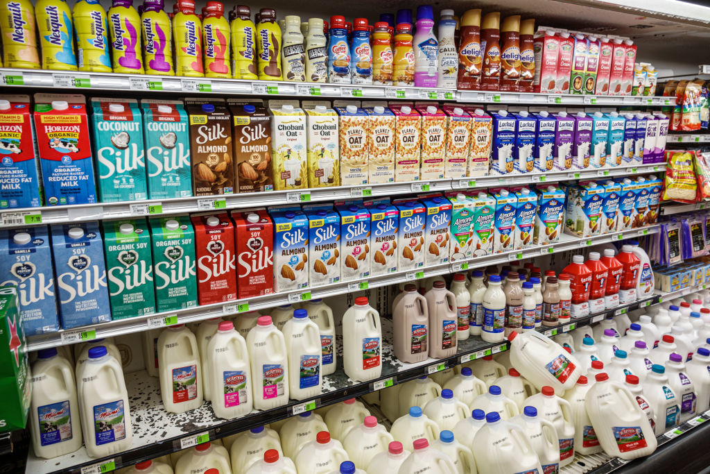 Supermarket shelves showing different types of milk, including oat milk, coconut milk, almond milk, and dairy milk