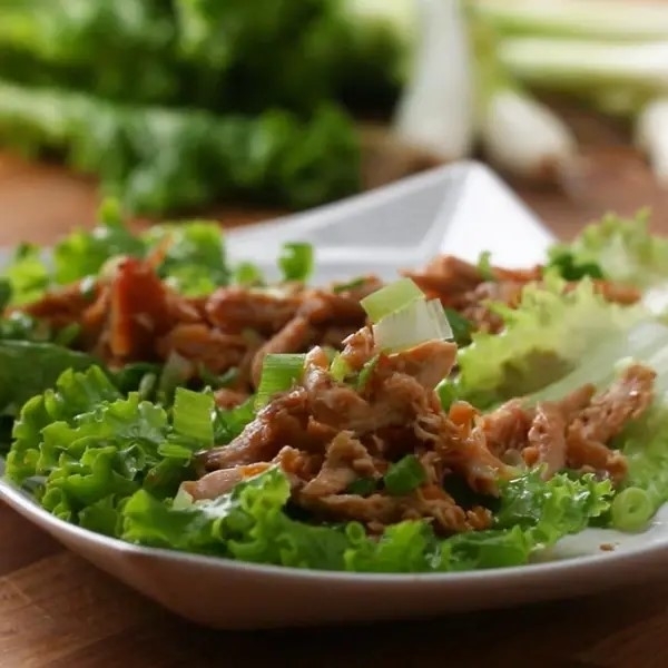 Pulled pork served on crisp lettuce leaves, garnished with chopped green onions, in a white dish